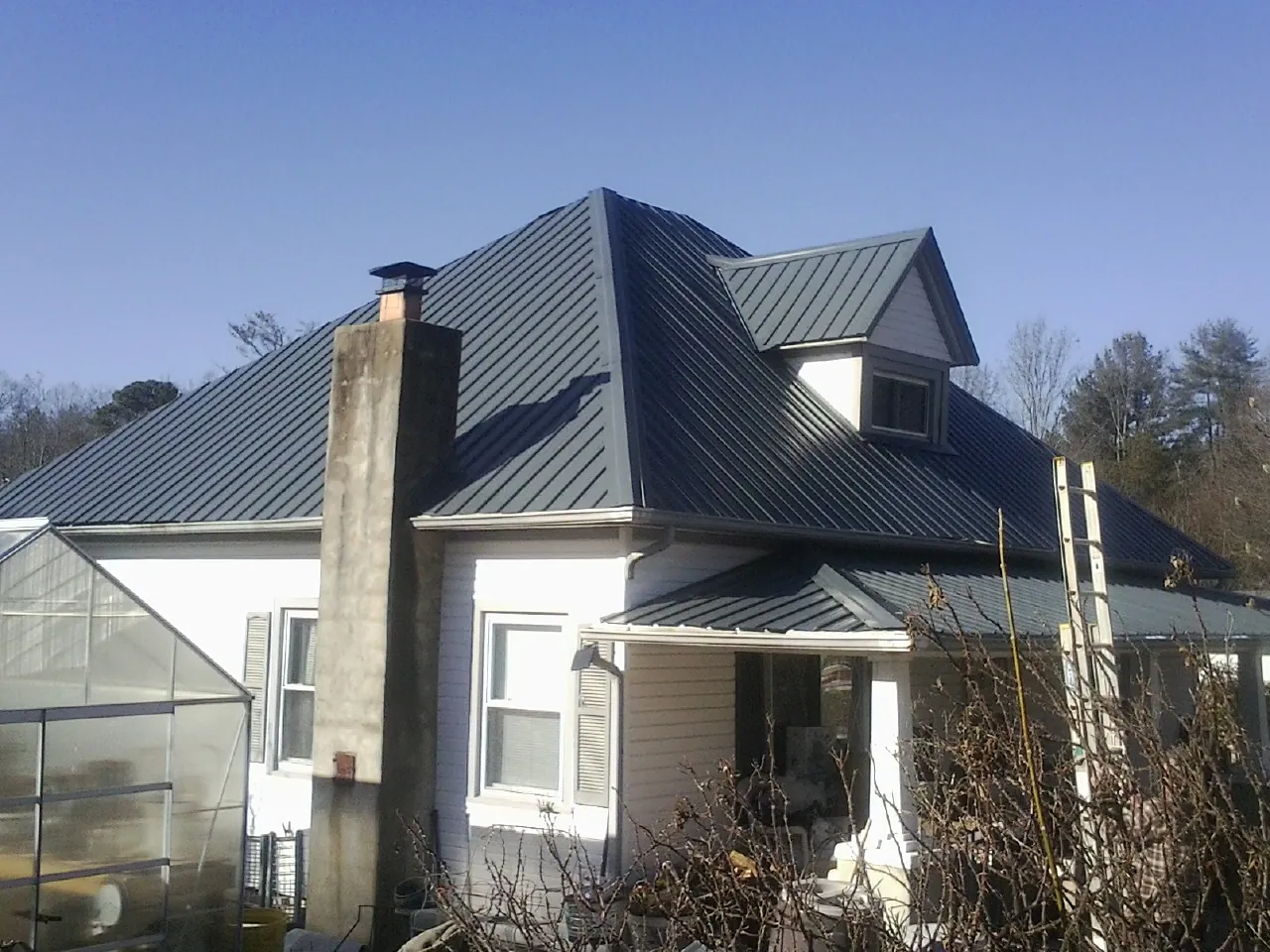 Dark blue standing seam metal roof on a white farmhouse with dormer — Slate & Tile Roof Repair by Roofing Brothers in Gastonia