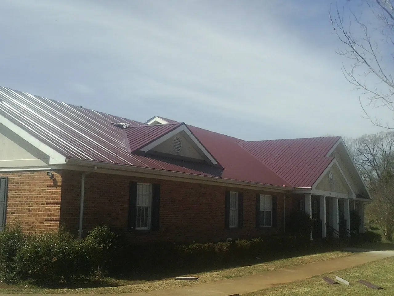 Red metal roof with gabled entries on a long brick building, from a Hail Damage Roof Repair job in Gastonia