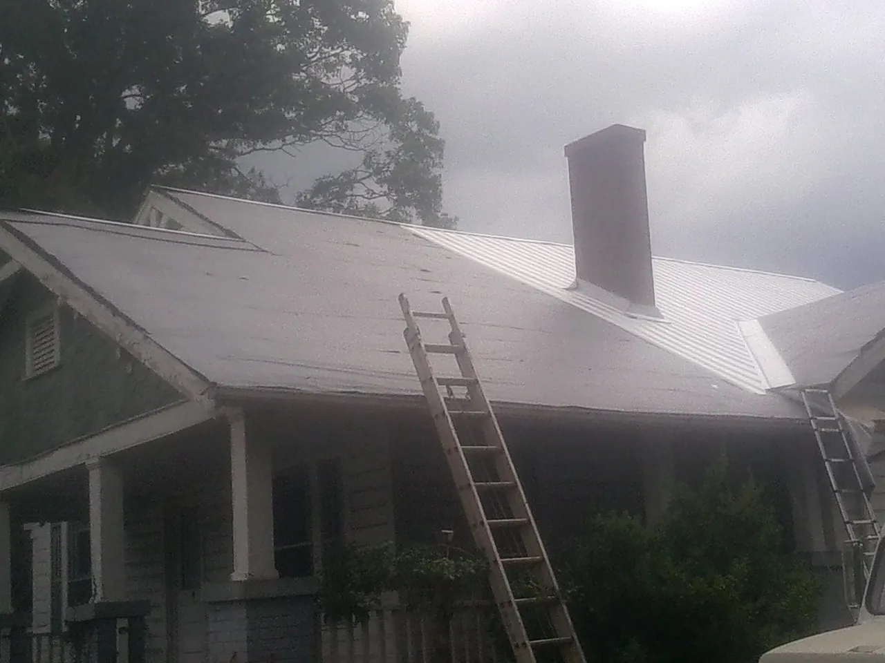 Ladders against a metal roof on an older home with a brick chimney in Gastonia