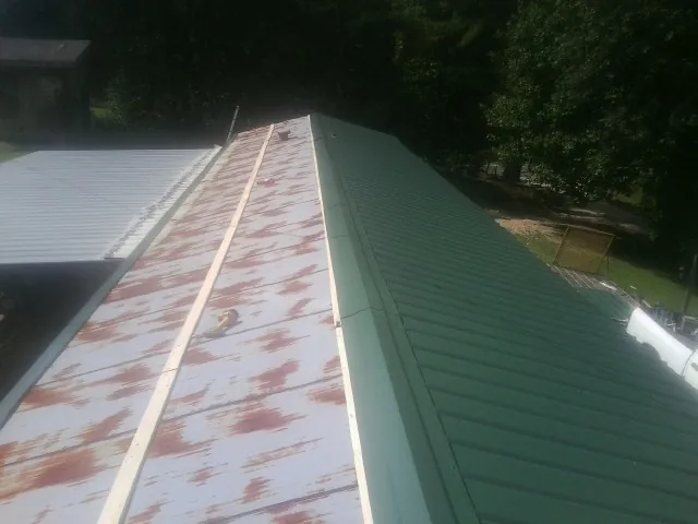 Old rusted panels beside newly installed green metal roofing — Wind Damage Roof Repair by Roofing Brothers in Gastonia