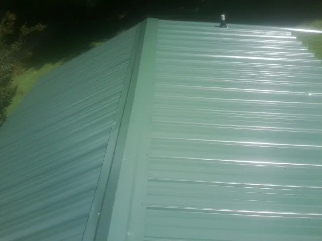 New green metal panels meeting at the ridge of a roof — Flat Roof Repair work by our crew in Gastonia