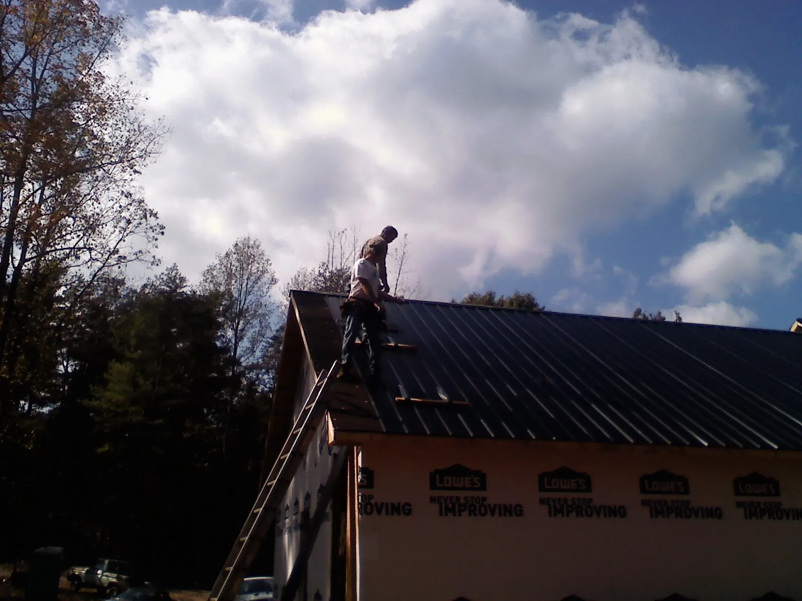 Roofer fastening dark metal panels high against a cloudy sky, from a Roof Inspection job in Gastonia