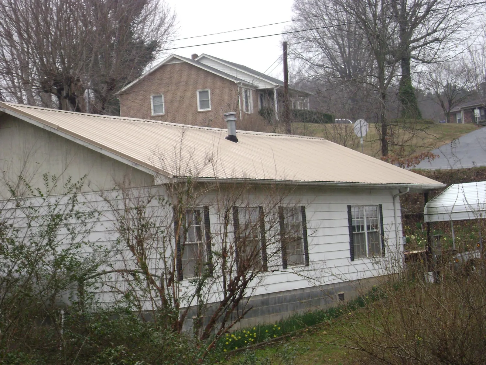 Tan metal roof on a white sided house set into a hillside — Commercial Roofing by Roofing Brothers in Gastonia