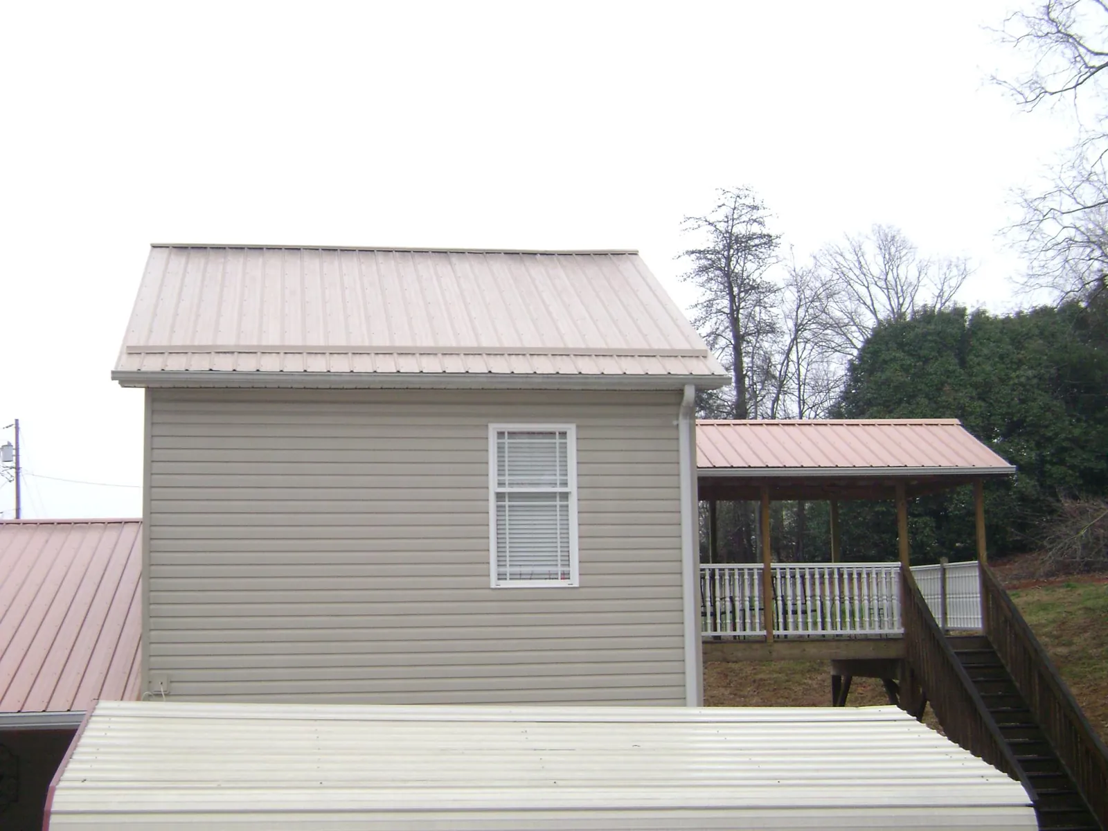 Tan metal roofs on a two story addition and attached porch, from a Roof Replacement job in Gastonia